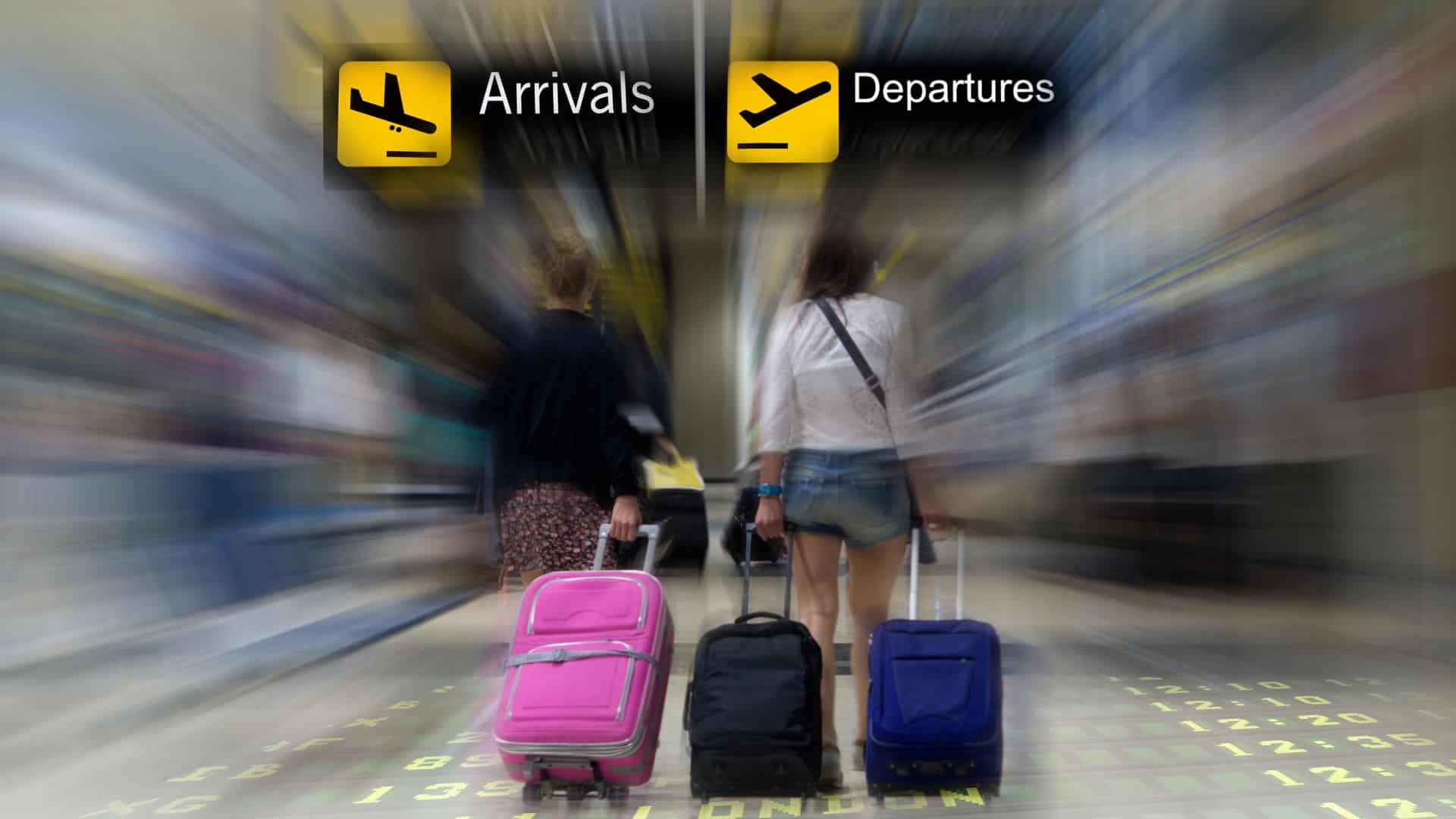 A motion shot of two women holding luggage standing in front of airport signs.