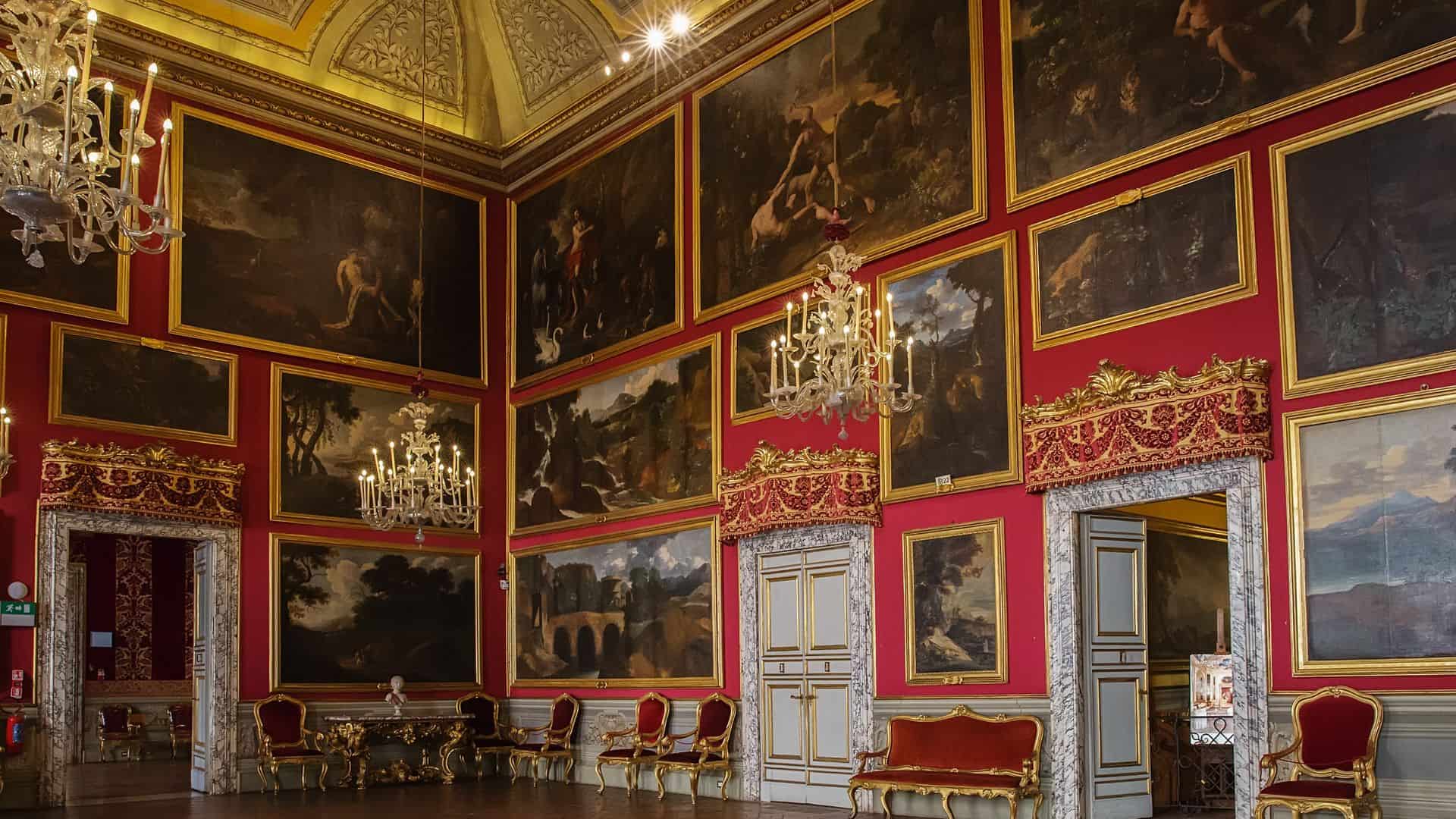 The interior of a red-walled and gilded room filled with paintings inside the Doria Pamphilj Gallery.