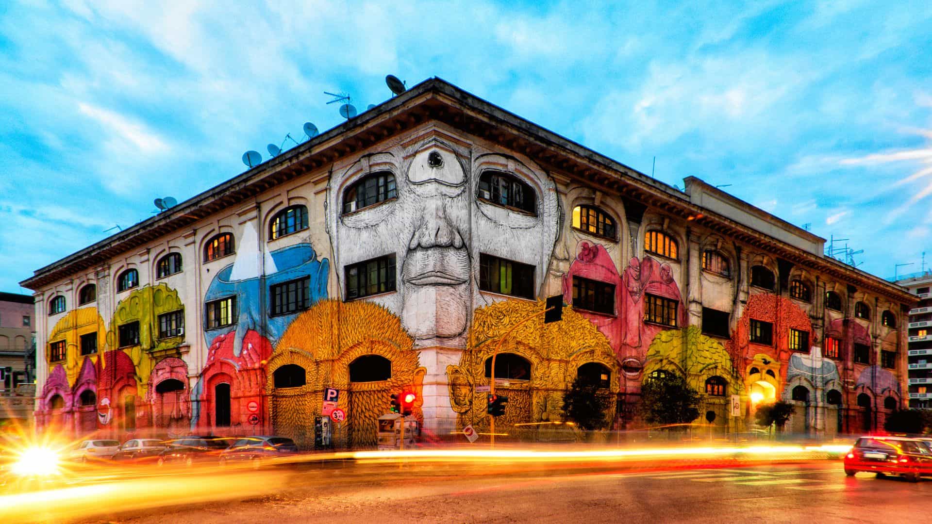 Cars pass by a building in Ostiense covered in street art.