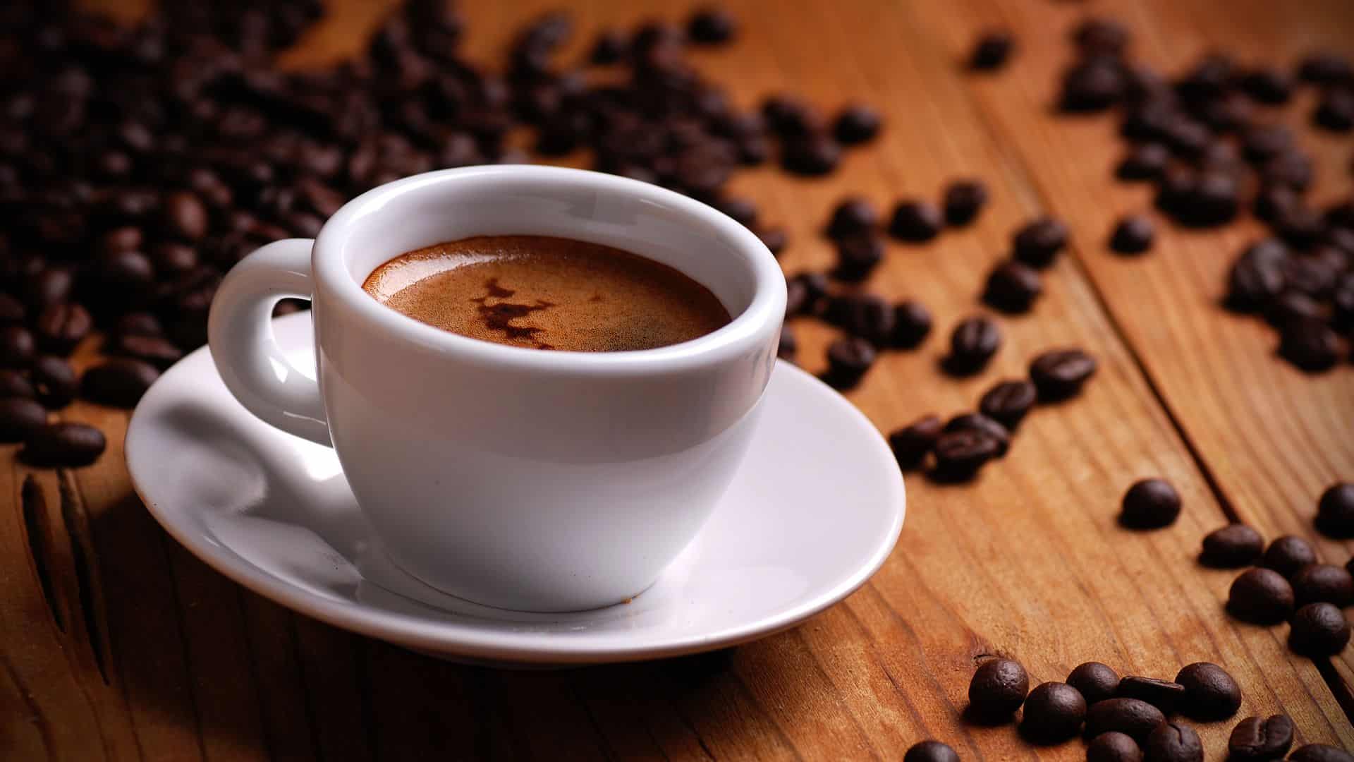 An espresso sits on a table surrounded by coffee beans.